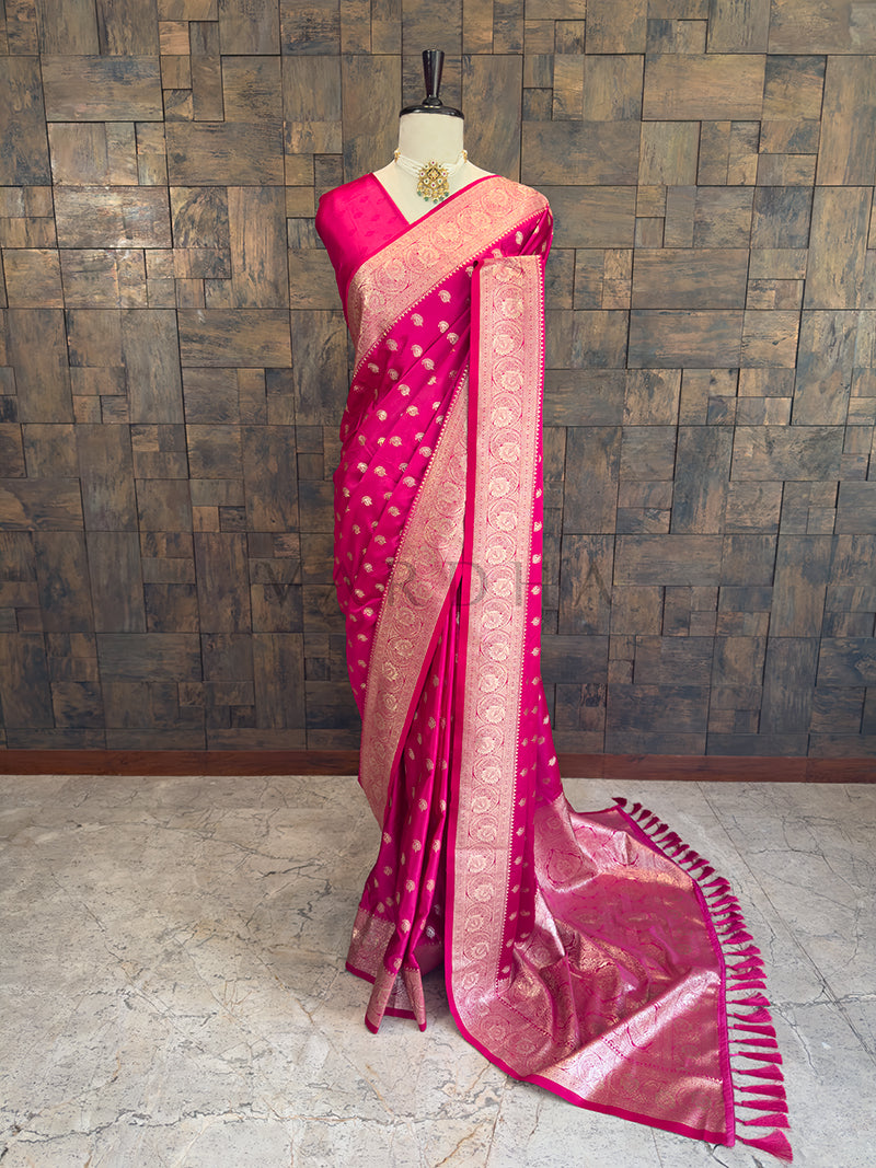 Pink saree with a pattern on a mannequin against a wooden paneled wall. Full front display of a rani pink satin silk saree featuring golden zari paisley bootis draped gracefully on a mannequin. Festive ethnic wear rani pink zari woven saree sweeping the floor, showcasing the heavily brocaded pallu and traditional patterns.