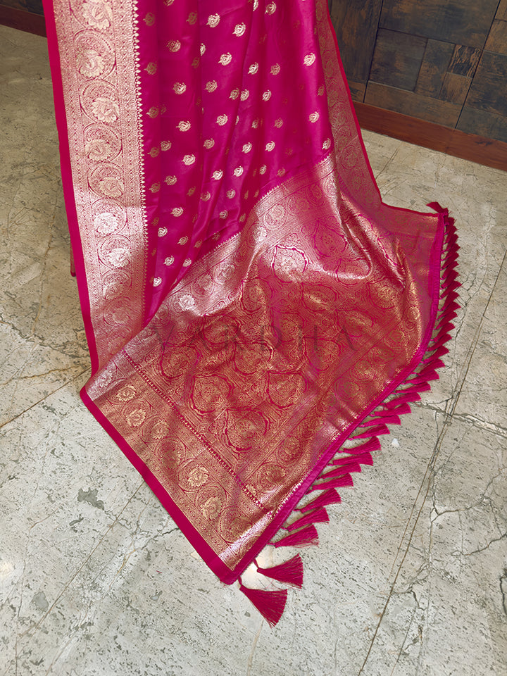 Pink saree with gold patterns on a marble floor Detailed floor view of the rich, densely woven golden zari pallu with matching tassels on a vibrant pink satin saree.