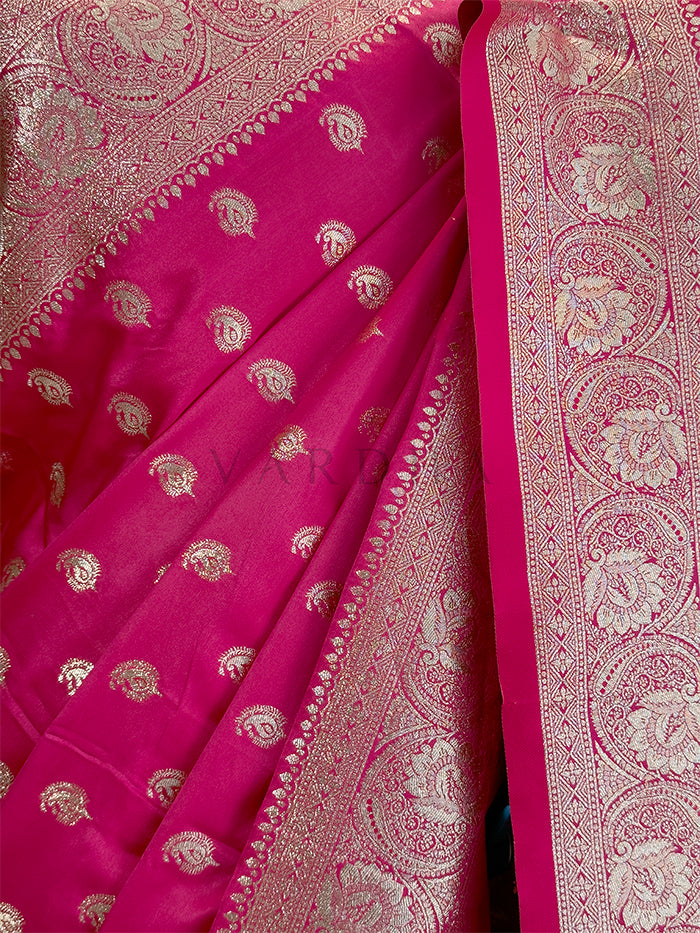 Pink saree with intricate white patterns on a dark background Close-up texture shot highlighting the woven paisley bootis and dense traditional zari border on a rani pink satin fabric.