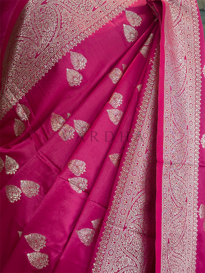 Pink saree with intricate gold patterns on a plain background Elegant drape and pleated look of the bright pink Banarasi-style satin silk saree with heavy zari border. Indian ethnic party wear rani pink saree displaying opulent paisley pallu details and a rich traditional aesthetic.