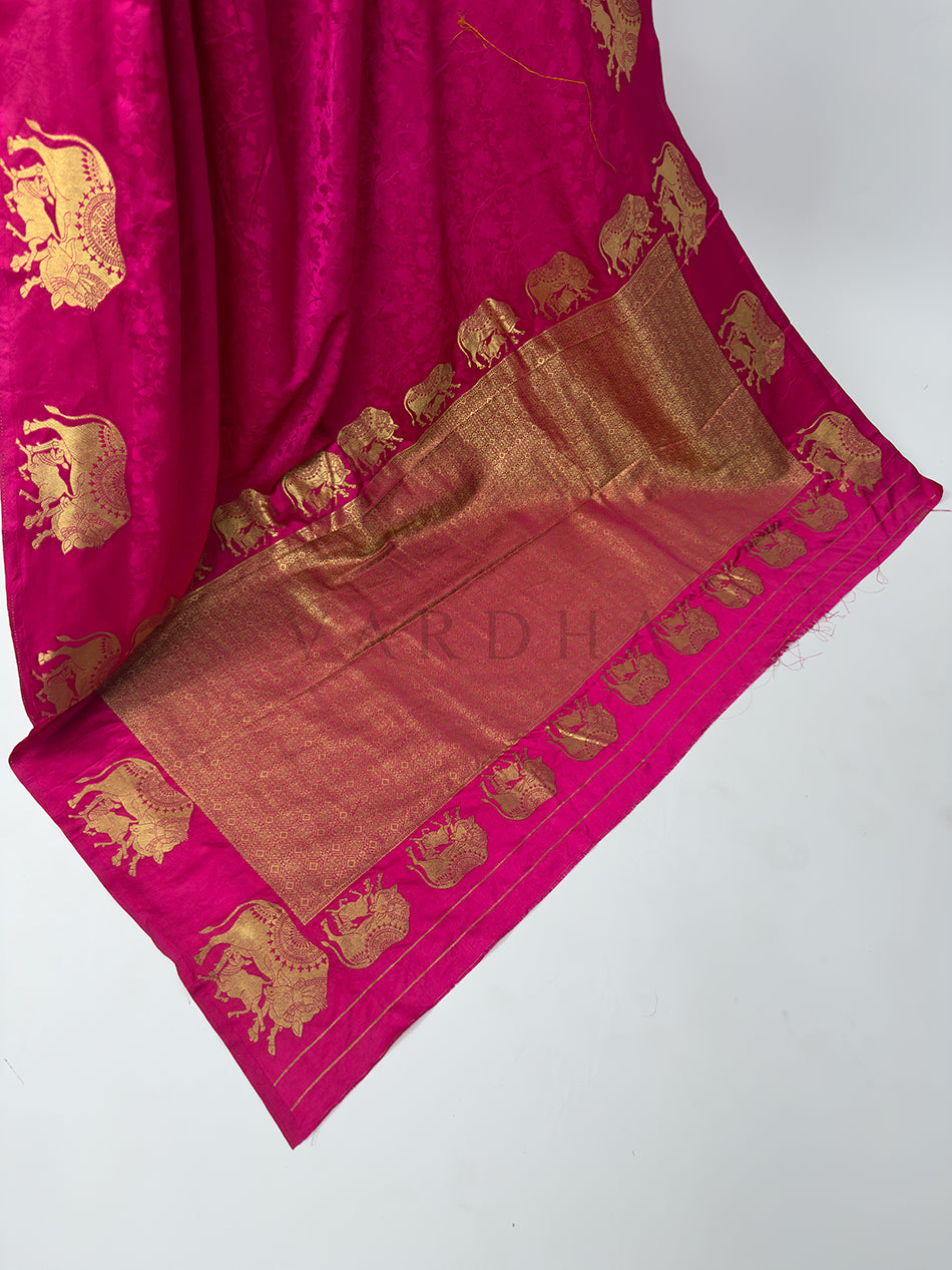 Pink saree with gold patterns on a white background A high-angle shot showcasing the grand, fully extended pallu of the Pink Satin Silk Saree spread out across the floor. The center of the palla features a heavy and dense geometric grid pattern woven entirely from gleaming gold zari threads. This luxurious weave is framed by a beautiful parade of marching elephant motifs, celebrating classic Banarasi handloom heritage.