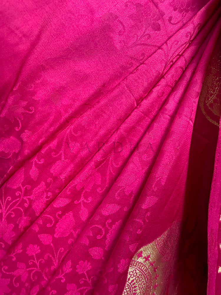 Close-up of a pink fabric with intricate patterns An extreme close-up view of the Pink Satin Silk Saree fabric, highlighting its rich texture and meticulous craftsmanship in sharp focus. The shot reveals the complex self-jacquard weaving that creates an embossed pattern of delicate floral leaves and vines across the glossy pink surface, seamlessly paired with the corner of a glittering metallic gold zari motif.