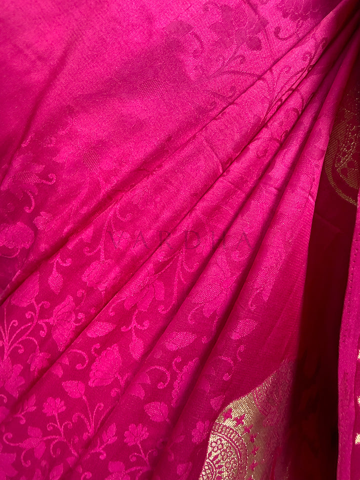 Close-up of a pink fabric with intricate patterns An extreme close-up view of the Pink Satin Silk Saree fabric, highlighting its rich texture and meticulous craftsmanship in sharp focus. The shot reveals the complex self-jacquard weaving that creates an embossed pattern of delicate floral leaves and vines across the glossy pink surface, seamlessly paired with the corner of a glittering metallic gold zari motif.