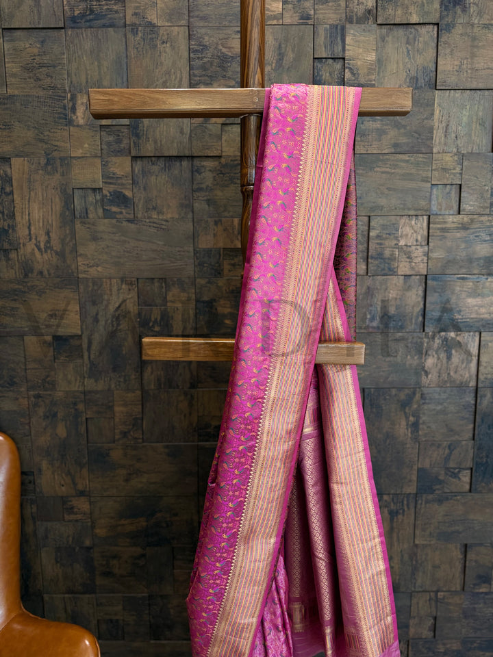 Pink satin saree with golden zari striped border and woven pallu, featuring intricate multicolor parrot motifs for festive styling