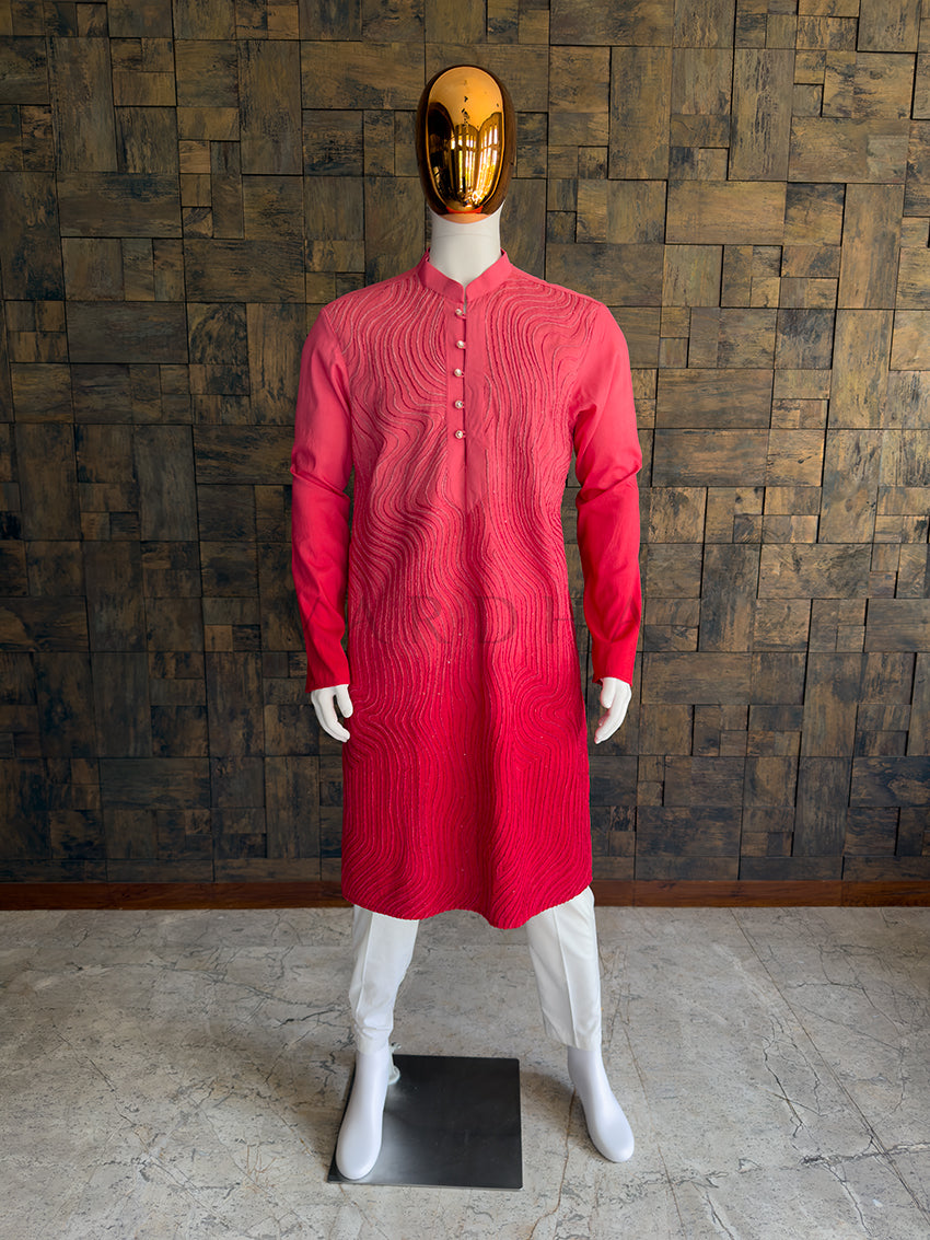Mannequin wearing a pink kurta with a gold mask against a wooden paneled wall. Front view of a man wearing a House of Vardha vibrant pink viscose kurta featuring an all-over swirling topographical cord embroidery.