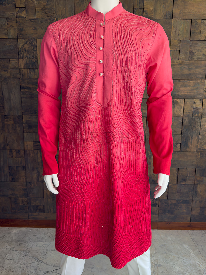 pink kurta with intricate patterns on a mannequin against a wooden paneled wall. Close-up of the bright pink men's festive kurta showcasing the textured wavy threadwork and jeweled decorative buttons.