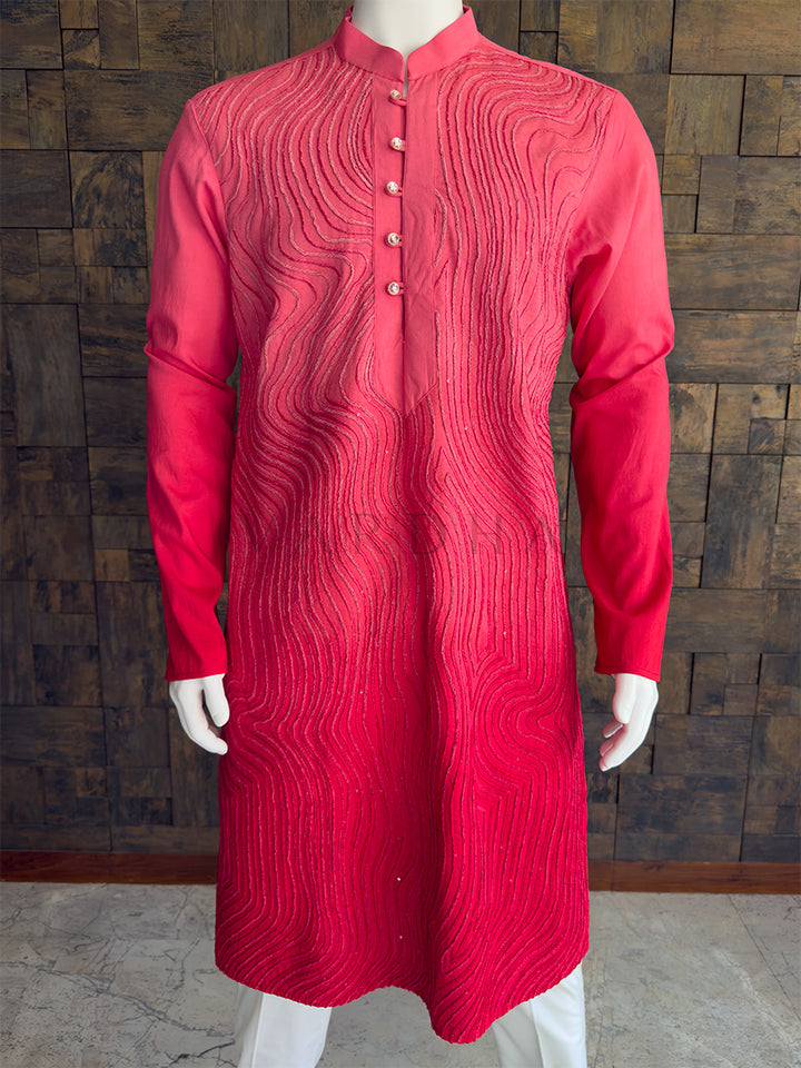 pink kurta with intricate patterns on a mannequin against a wooden paneled wall. Close-up of the bright pink men&