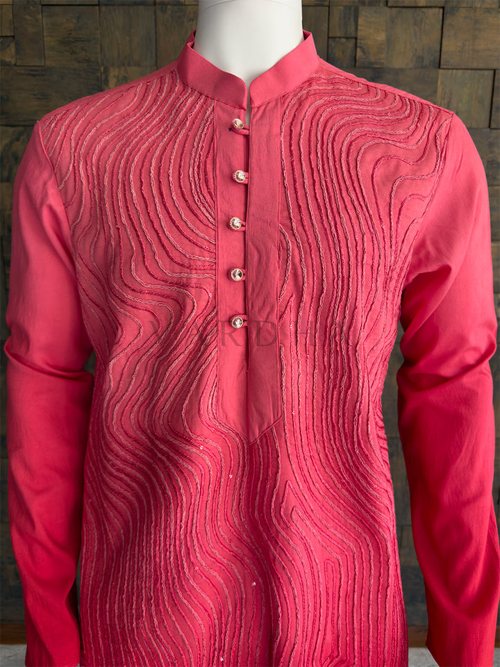 Red kurta with intricate patterns on a wooden background. Detailed view of the premium rhinestone buttons and the intricate cording on the mandarin collar of the magenta kurta.