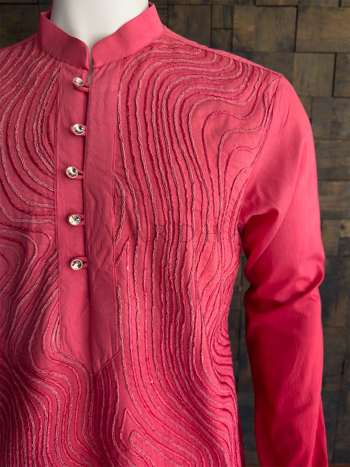 Pink kurta with intricate patterns on a wooden background. Side profile of the pink patterned viscose kurta for men, highlighting the luxurious drape and full sleeves for evening wear. 