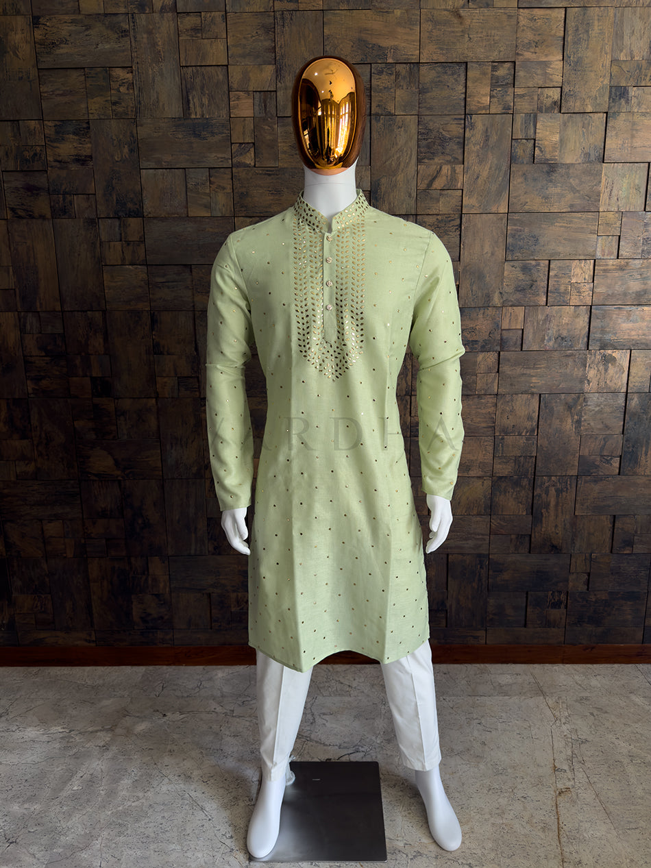Mannequin wearing a light green kurta with white pants against a wooden paneled wall. Men&