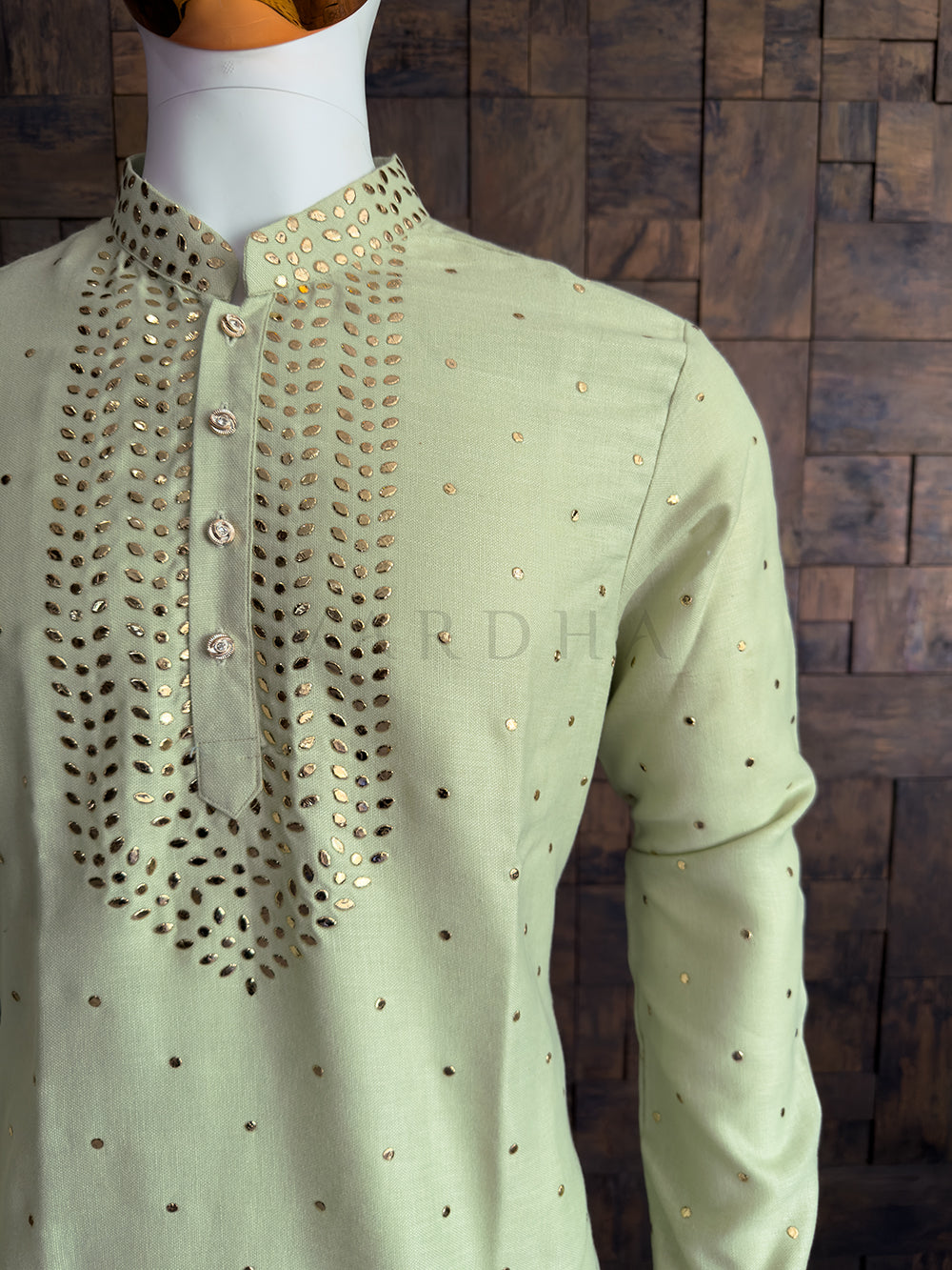 Light green shirt with intricate black embroidery on a wooden background. Stylish pista green cotton kurta for men with mandarin collar and gold mukaish handwork