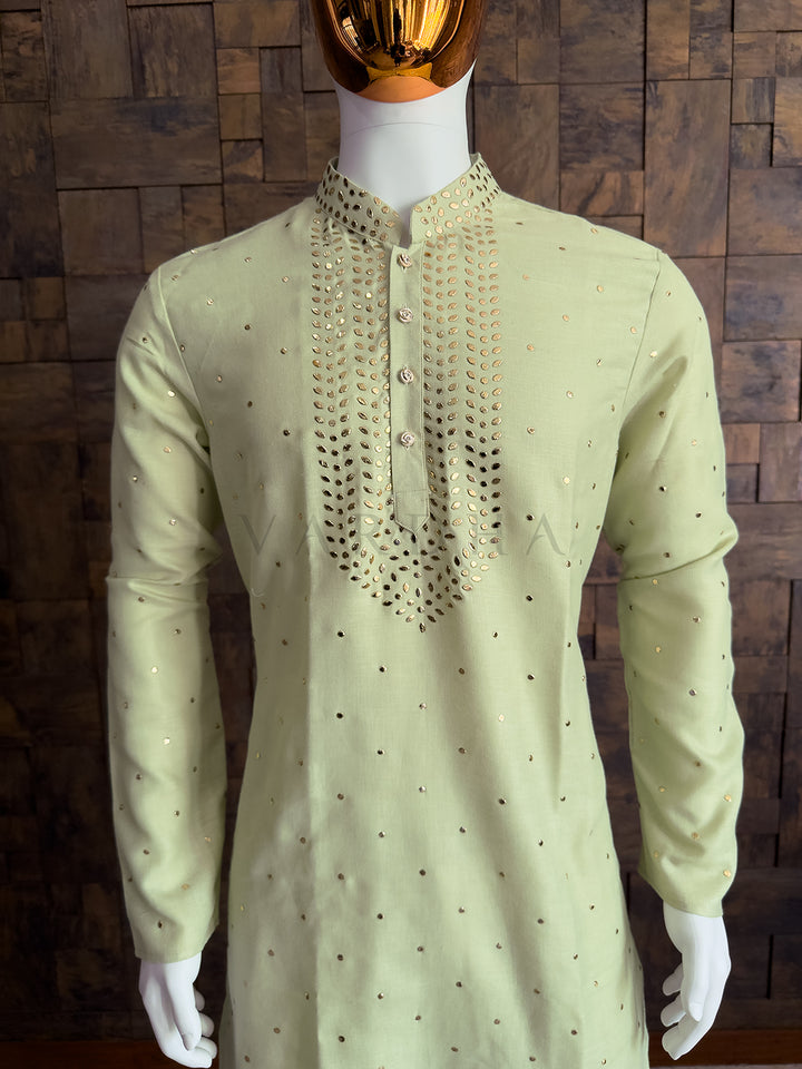 Light green kurta with intricate embroidery on a mannequin against a wooden wall. Premium pista green ethnic kurta with gold mukaish embellishments and classic straight fit design