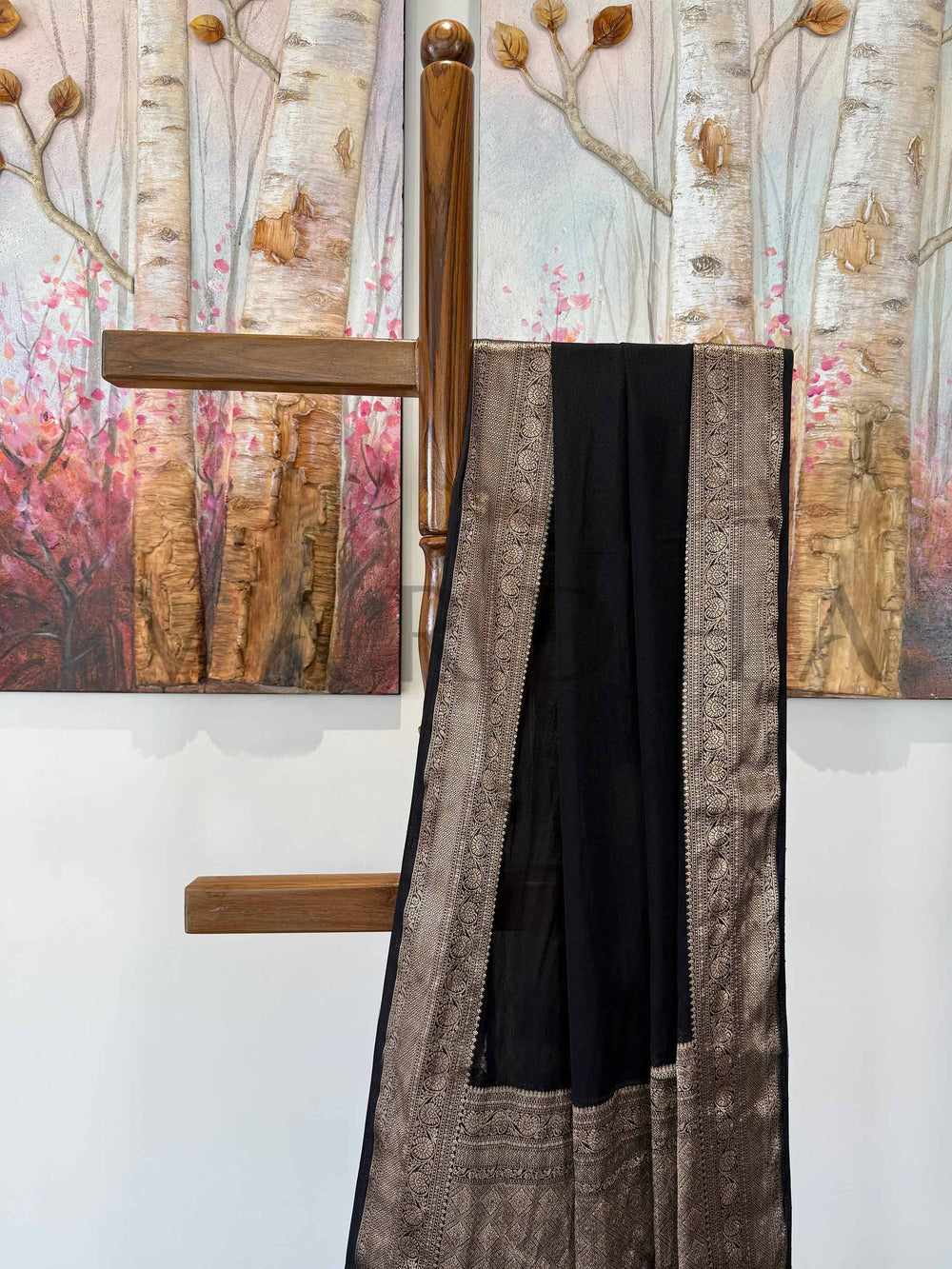 A feather-light black saree with shimmering gold zari embroidery, elegantly arranged against a minimalistic backdrop. The smooth drape and intricate craftsmanship add to its regal charm.