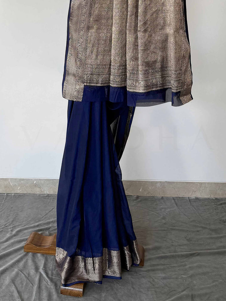 An exquisite blue saree in feather-soft georgette, featuring a beautifully woven gold zari border. Draped stylishly, this saree showcases its lightweight texture and regal color, perfect for special occasions.