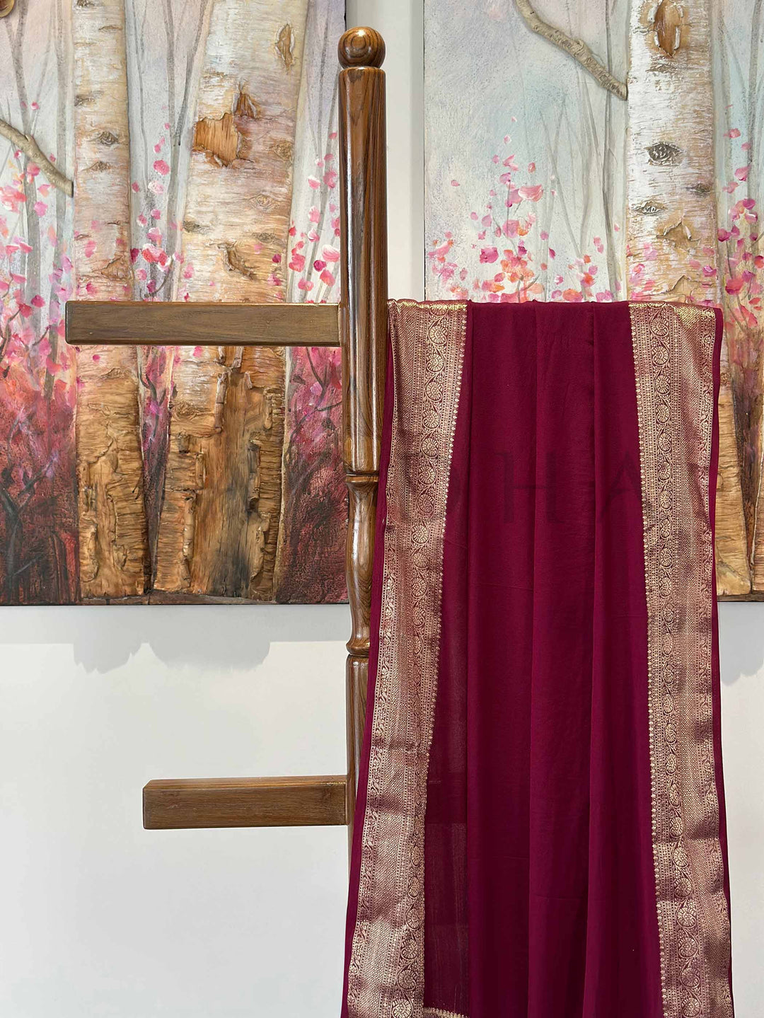 An exquisite deep wine-colored saree in feather-soft georgette, featuring a detailed gold zari border. Elegantly arranged, this saree highlights its lightweight texture and classic beauty, ideal for special events