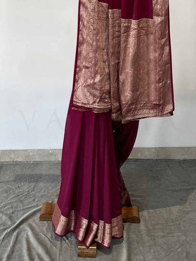 A rich wine georgette saree with shimmering gold zari embroidery, artistically draped to showcase its graceful fall and intricate detailing. The saree exudes opulence, making it a stunning choice for celebrations.