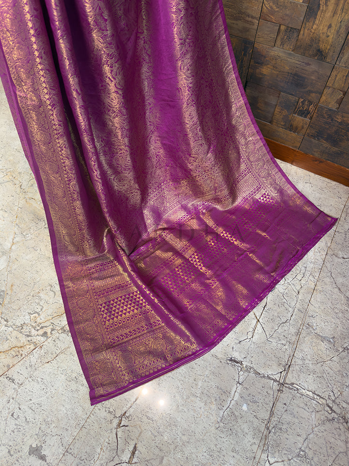 The elaborate pallu of a magenta Kanjivaram silk saree spread out, featuring striking geometric patterns, traditional motifs, and extensive golden zari weaving.