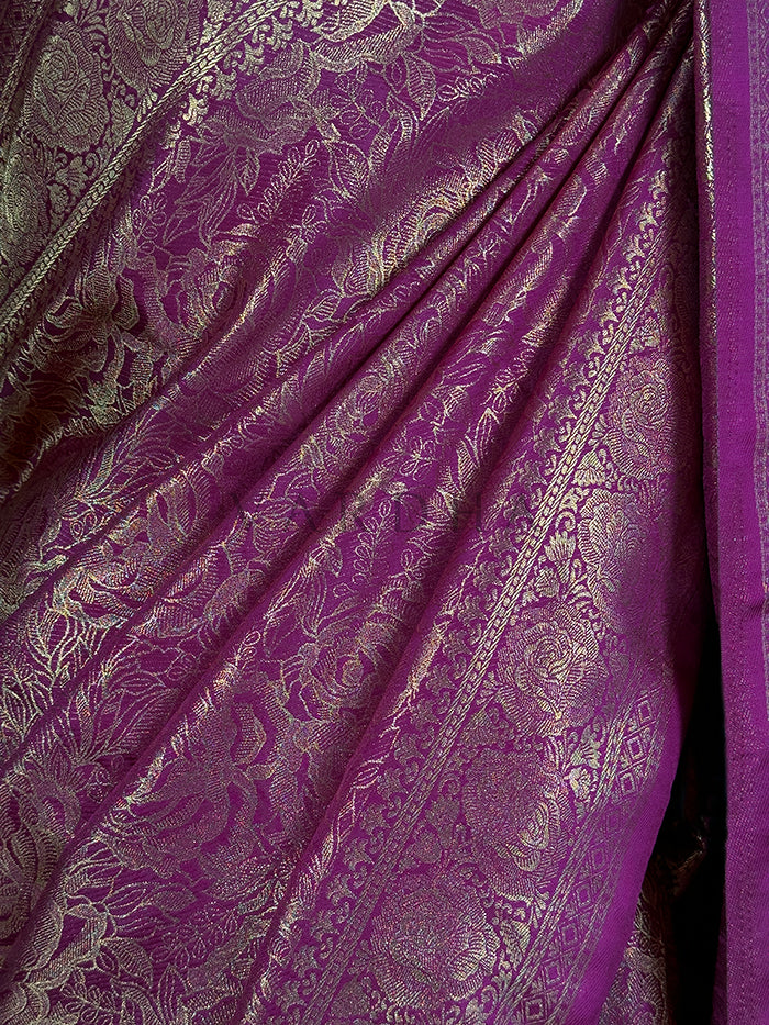 Extreme close-up of the magenta Kanjivaram art silk fabric, emphasizing the detailed craftsmanship and intricate golden zari weaving of traditional floral and vine motifs.