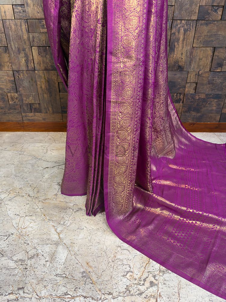 Detailed view of the cascading pleats and lower drape of a magenta Kanjivaram art silk saree, displaying the heavy golden zari border and rich texture flowing to the floor.