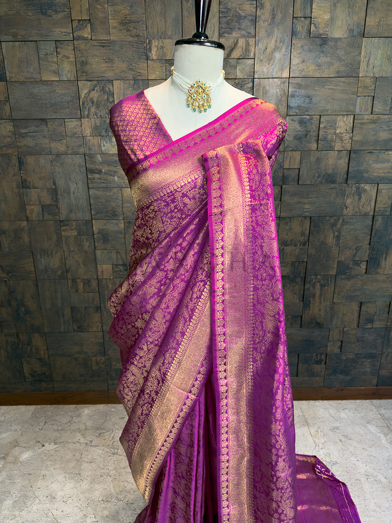 Purple saree with gold patterns on a mannequin against a wooden paneled wall. House of Vardha deep purple Kanjivaram Silk Saree with heavy gold zari craftsmanship, showcasing the pallu featuring traditional South Indian paisley and floral motifs. We offer Ready to wear, Pre drape service, Saree Add on, Custom Stitched Blouse, Fall and Edging, and Gift Packaging at Complimentary Price!