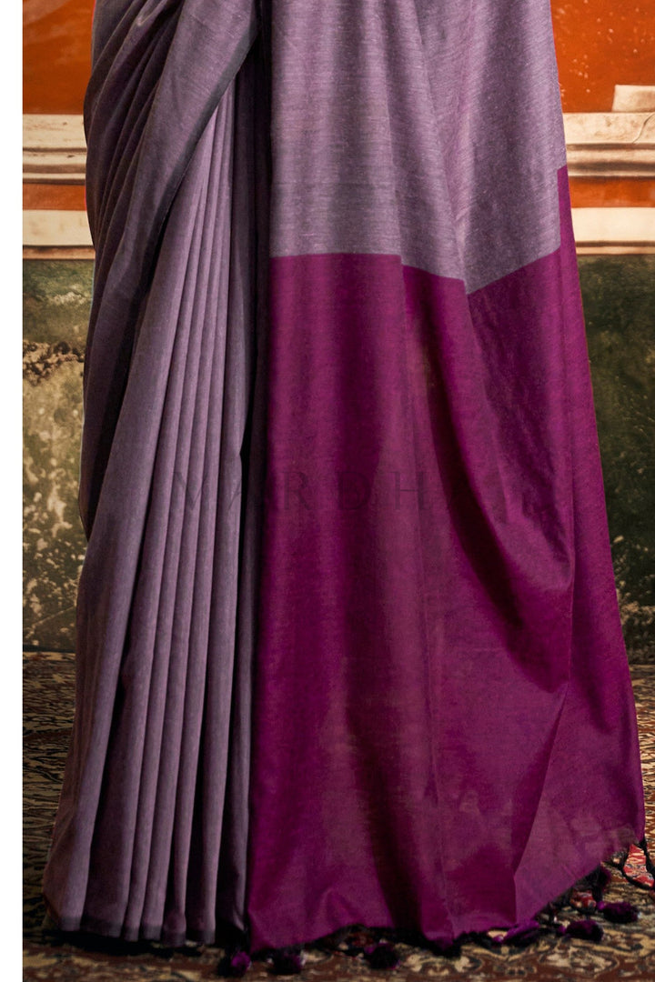 Purple and gray saree draped over a decorative background Detailed fabric close-up of the purple mal cotton saree highlighting the striking dark magenta contrast pallu and pleated texture.