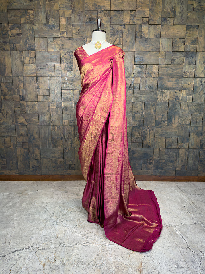 Pink saree with gold border on a mannequin against a textured wall. House of Vardha Rani Pink Kanjivaram Silk Saree featuring intricate Gold Zari woven floral and vine motifs, elegantly draped on a mannequin. We offer Ready to wear, Pre drape service, Saree Add on, Custom Stitched Blouse, Fall and Edging, Gift Packaging at Complimentary Price!