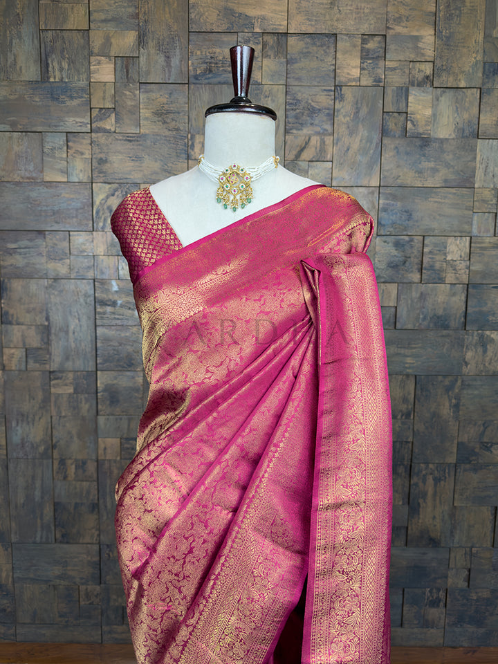 Pink saree with gold border on a mannequin against a brick wall. Lustrous Rani Pink Kanjivaram Silk Saree by House of Vardha showcasing exquisite traditional Gold Zari craftsmanship and a rich texture. We offer Ready to wear, Pre drape service, Saree Add on, Custom Stitched Blouse, Fall and Edging, Gift Packaging at Complimentary Price!
