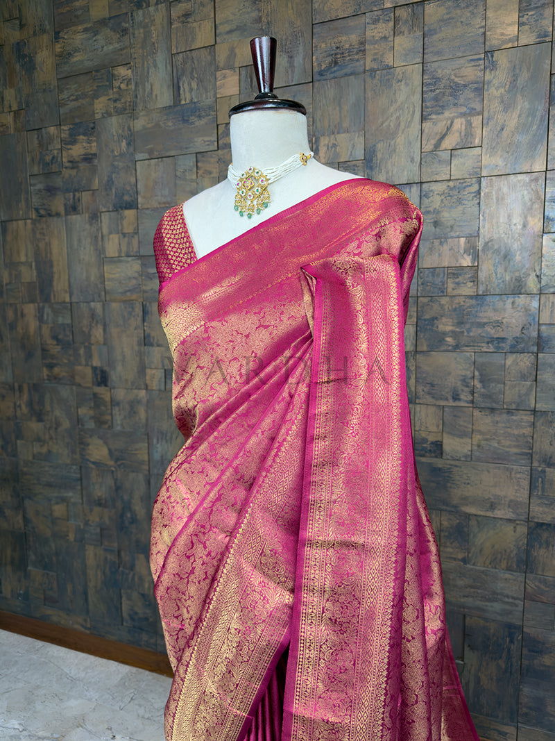 Pink saree with gold patterns on a mannequin against a textured wall. Close-up view of the House of Vardha Rani Pink Kanjivaram Silk Saree highlighting the detailed Gold Zari motifs and the beautifully woven traditional border. We offer Ready to wear, Pre drape service, Saree Add on, Custom Stitched Blouse, Fall and Edging, Gift Packaging at Complimentary Price!