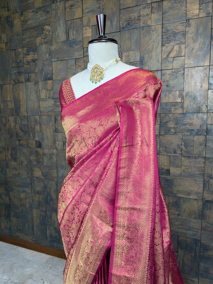 Pink saree with gold patterns on a mannequin against a textured wall. Close-up view of the House of Vardha Rani Pink Kanjivaram Silk Saree highlighting the detailed Gold Zari motifs and the beautifully woven traditional border. We offer Ready to wear, Pre drape service, Saree Add on, Custom Stitched Blouse, Fall and Edging, Gift Packaging at Complimentary Price!