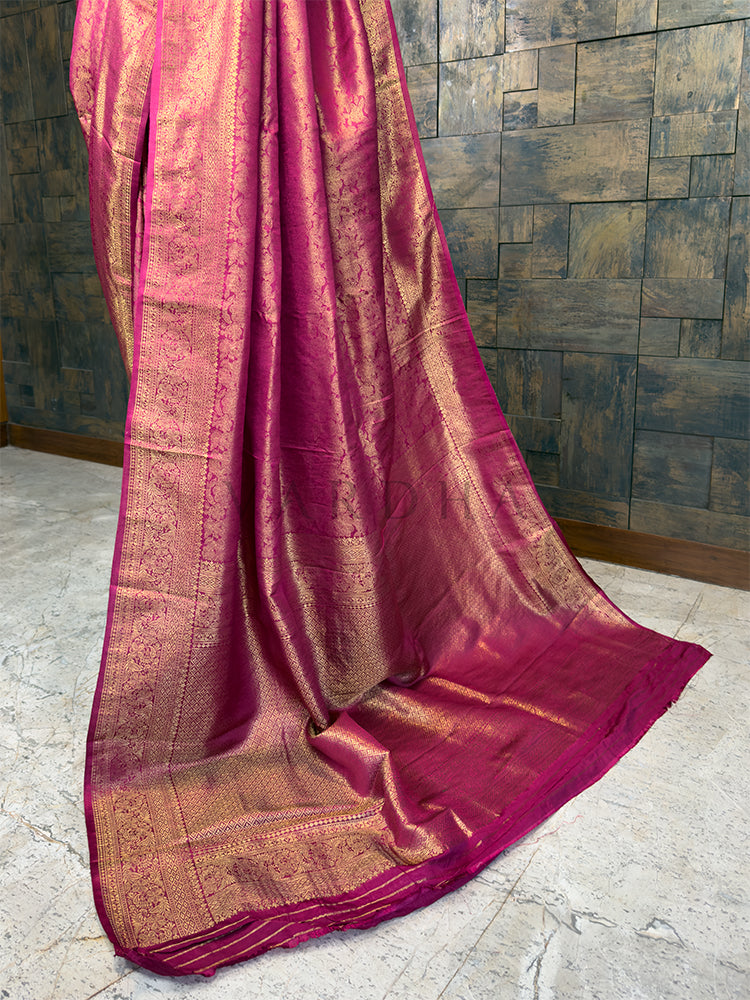 Pink saree with gold patterns draped over a textured wall. Elegant Rani Pink festive Kanjivaram Silk Saree from House of Vardha with radiant Gold Zari weave, perfect for weddings and special occasions. We offer Ready to wear, Pre drape service, Saree Add on, Custom Stitched Blouse, Fall and Edging, Gift Packaging at Complimentary Price!