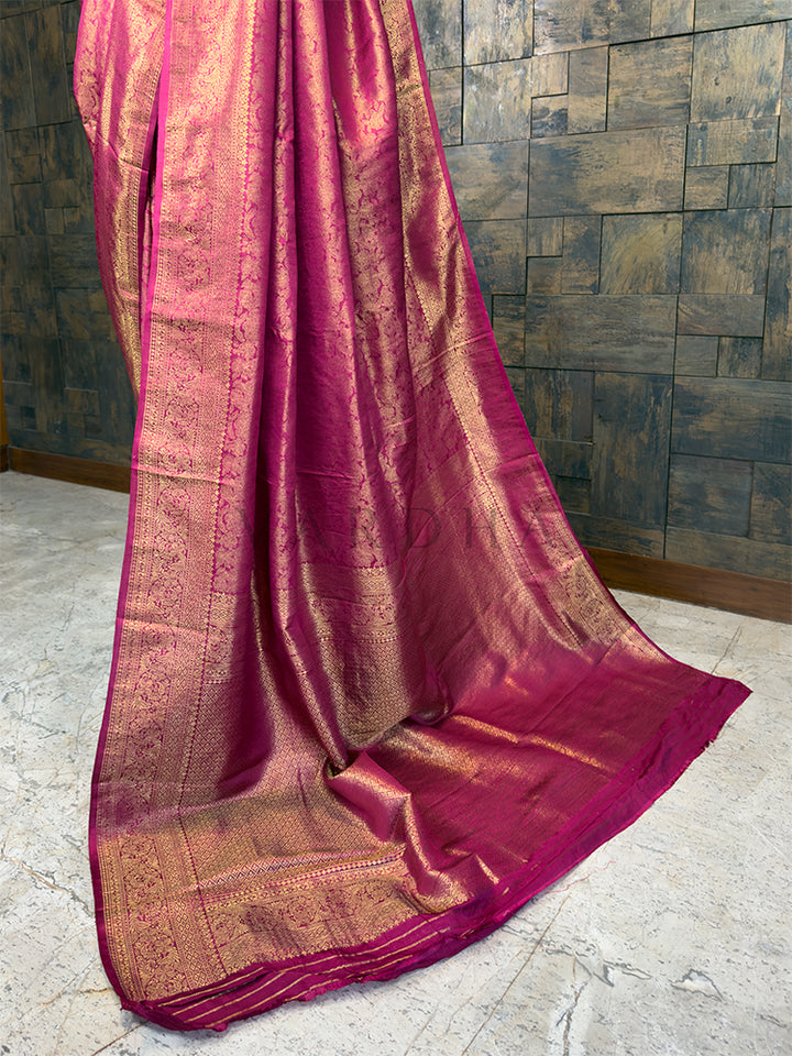 Pink saree with gold patterns draped over a textured wall. Elegant Rani Pink festive Kanjivaram Silk Saree from House of Vardha with radiant Gold Zari weave, perfect for weddings and special occasions. We offer Ready to wear, Pre drape service, Saree Add on, Custom Stitched Blouse, Fall and Edging, Gift Packaging at Complimentary Price!