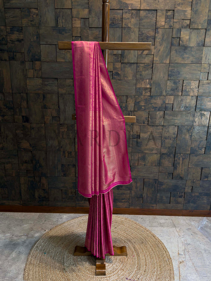 Rani pink Kanjivaram art silk saree on stand with golden zari floral jaal and geometric brocade borders, rich pallu and crisp pleats, traditional festive saree. House of Vardha designer Rani Pink Kanjivaram Silk Saree featuring traditional Gold Zari buttis across the body and a heavy, decorative pallu. We offer Ready to wear, Pre drape service, Saree Add on, Custom Stitched Blouse, Fall and Edging, Gift Packaging at Complimentary Price!