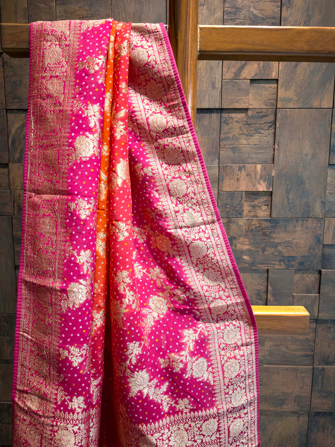 Pink and orange patterned fabric draped over a wooden rod against a stone wall.