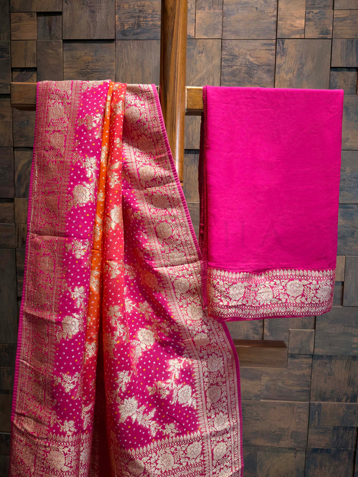 Two pink sarees with intricate patterns draped over a wooden rod against a wooden paneled wall.