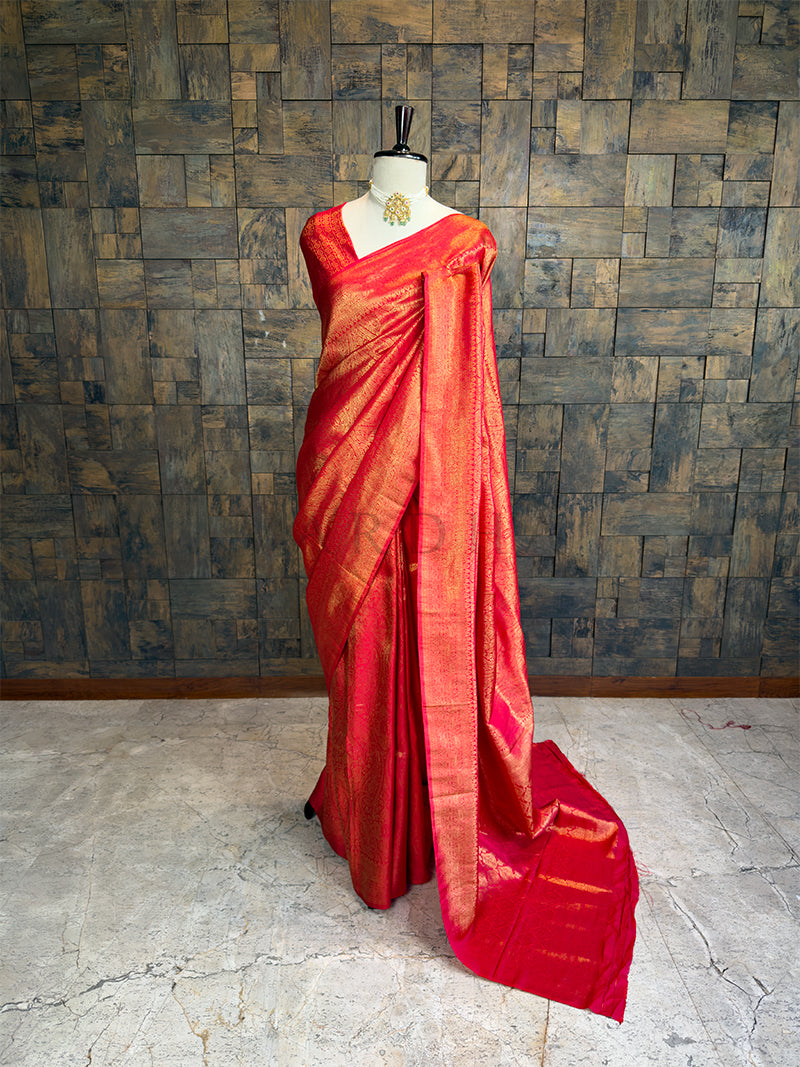 Red saree with gold border on a mannequin against a textured wall. House of Vardha Elegant Deep Red Silk Saree with Heavy Gold Zari Weaving, Wedding Collection
