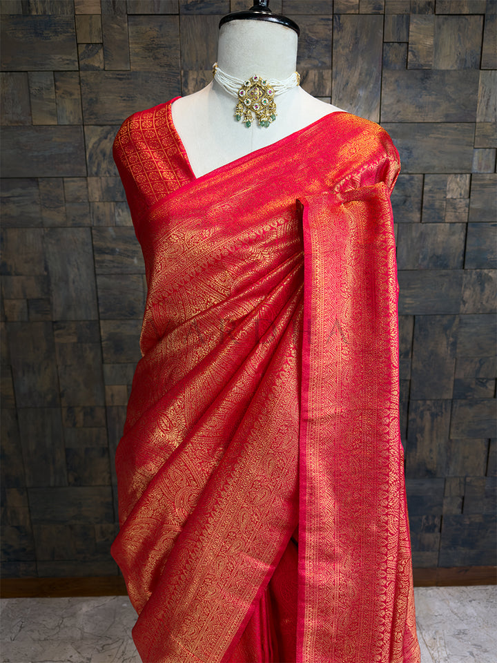 Red saree with gold patterns on a mannequin against a textured wall. Handwoven Red Silk Saree with Intricate Gold Zari Paisley (Kalki) and Floral Motifs, House of Vardha