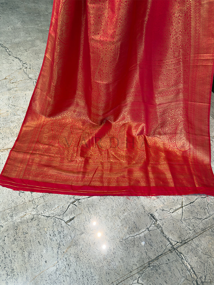Red fabric with intricate patterns on a textured surface Luxurious authentic Kanjivaram Indian wedding saree in vibrant red from House of Vardha with extensive gold brocade.