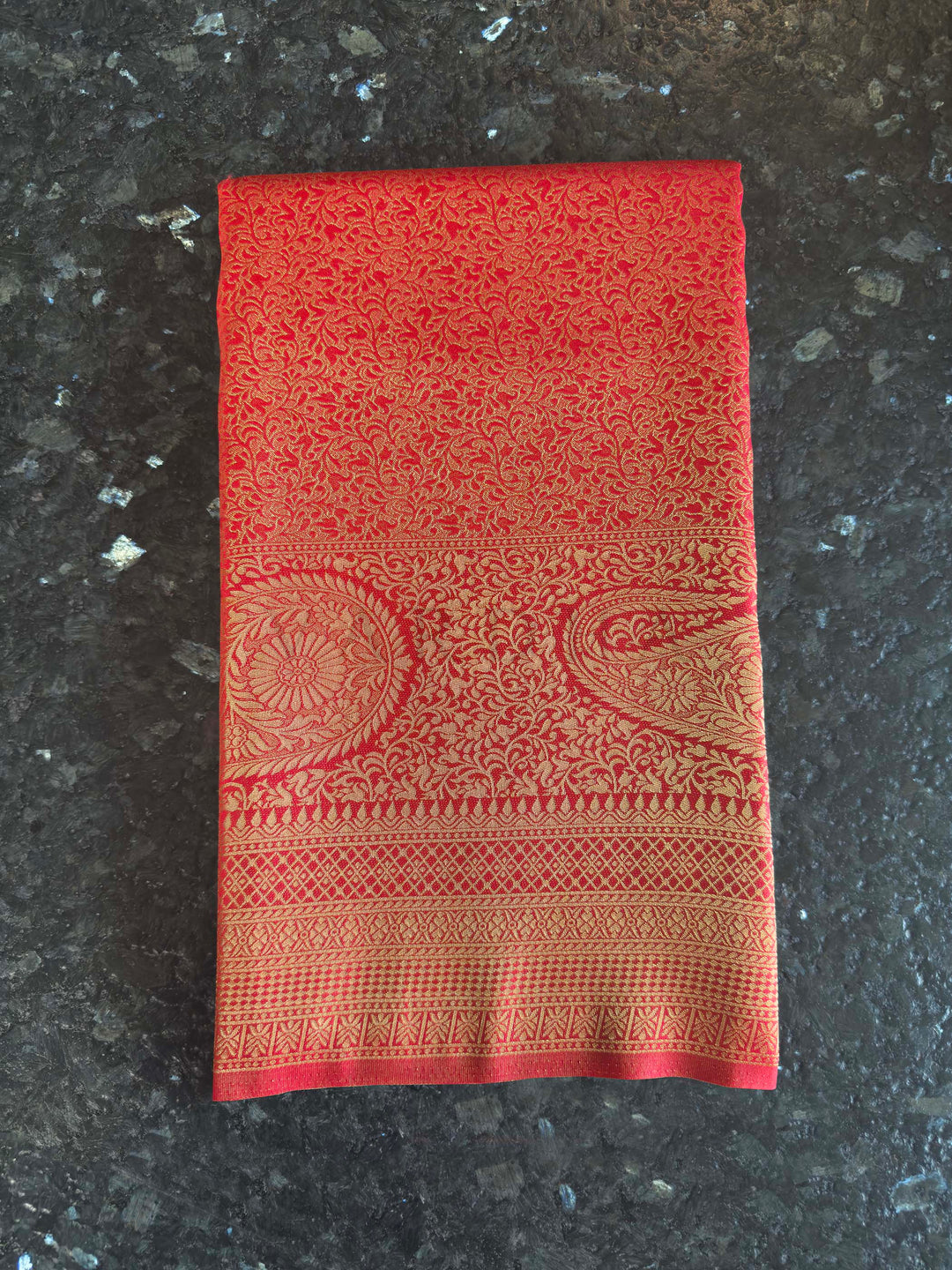 Red Golden Zari Kanjivaram Silk Saree House of Vardha. House of Vardha traditional bright red and gold Kanjivaram silk saree displaying a detailed heavy zari border against a textured backdrop.