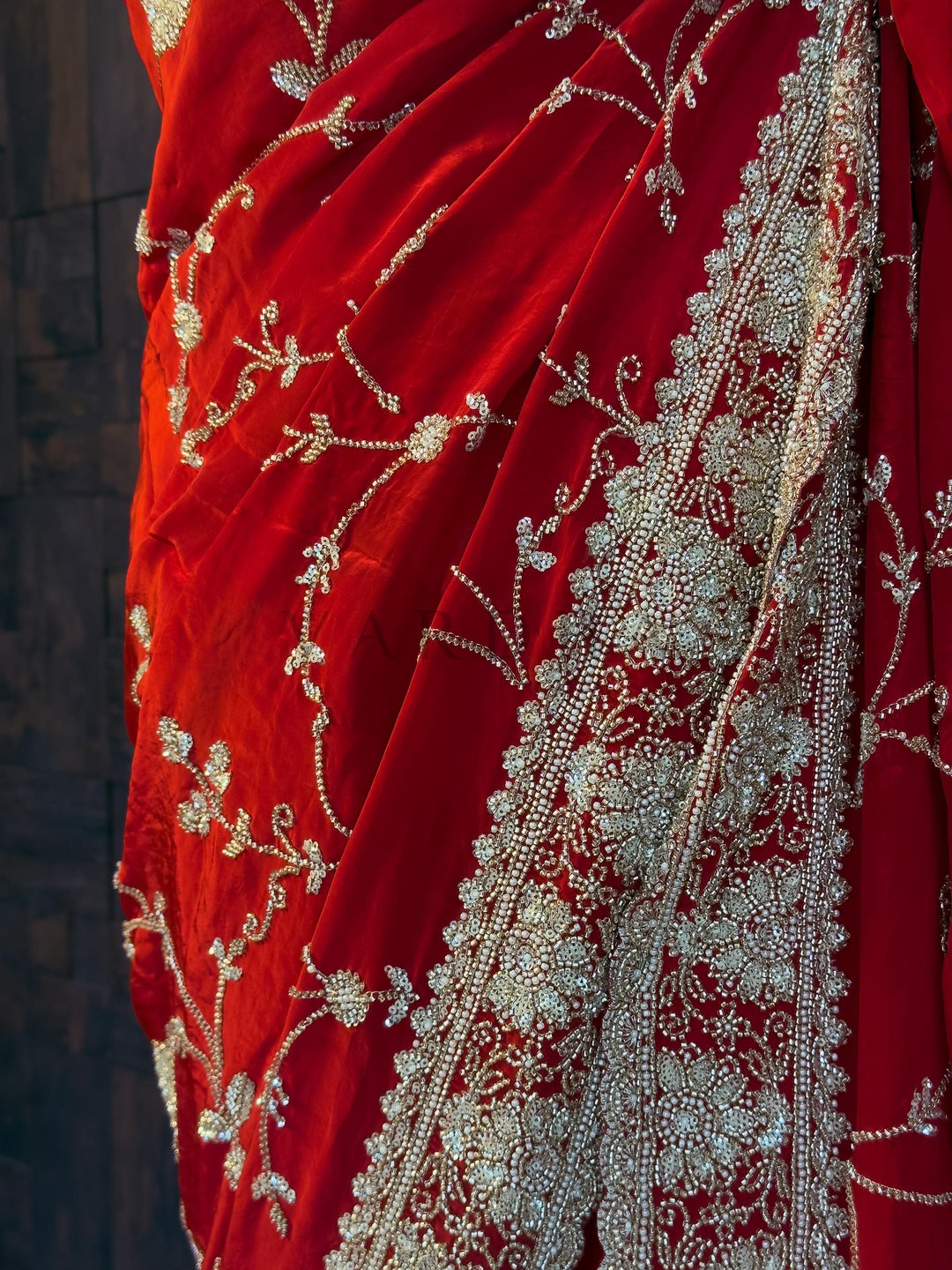 Red saree with intricate white embroidery on a dark background. House of Vardha designer Red Satin Crepe Saree showcasing a scalloped border intricately embellished with Silver Cutdana &amp; Floral Zircon Handwork and a stunning trailing pallu. We offer Ready to wear, Pre drape service, Saree Add on, Custom Stitched Blouse, Fall and Edging, Gift Packaging at Complimentary Price!