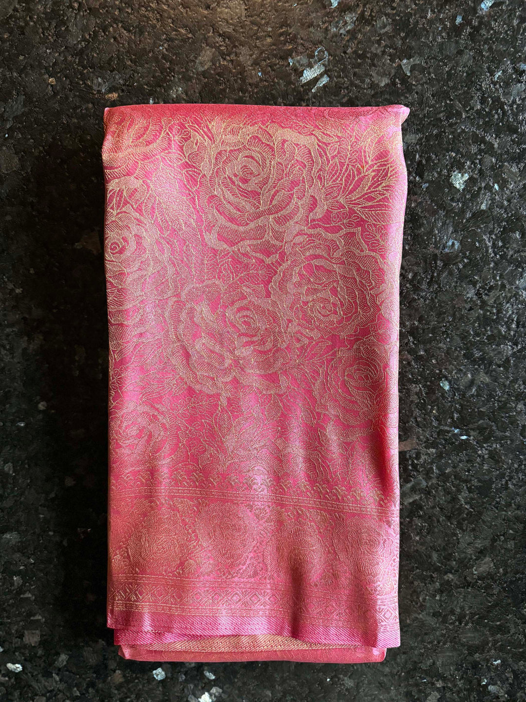Pink fabric with floral patterns on a dark surface Rich golden zari pallu of rose pink Kanjivaram saree with traditional motifs