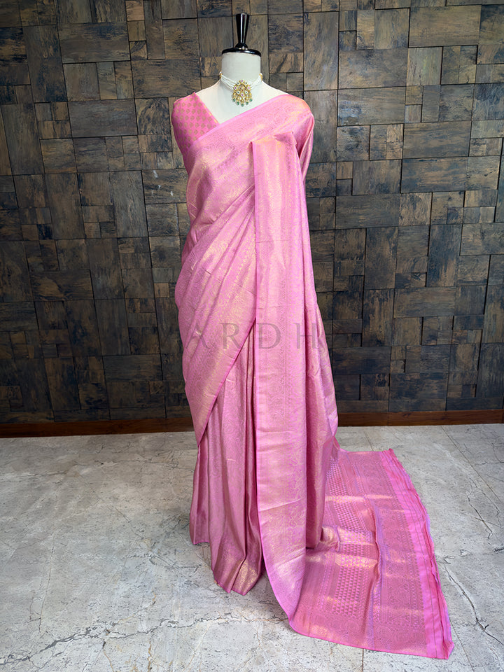 House of Vardha Rose Pink Golden Zari Kanjivaram Silk Saree featuring delicate all-over floral motifs draped on a mannequin. We offer Ready to wear, Pre drape service, Saree Add on, Custom Stitched Blouse, Fall and Edging, Gift Packaging at Complimentary Price!. Pink saree on a mannequin against a textured wall background