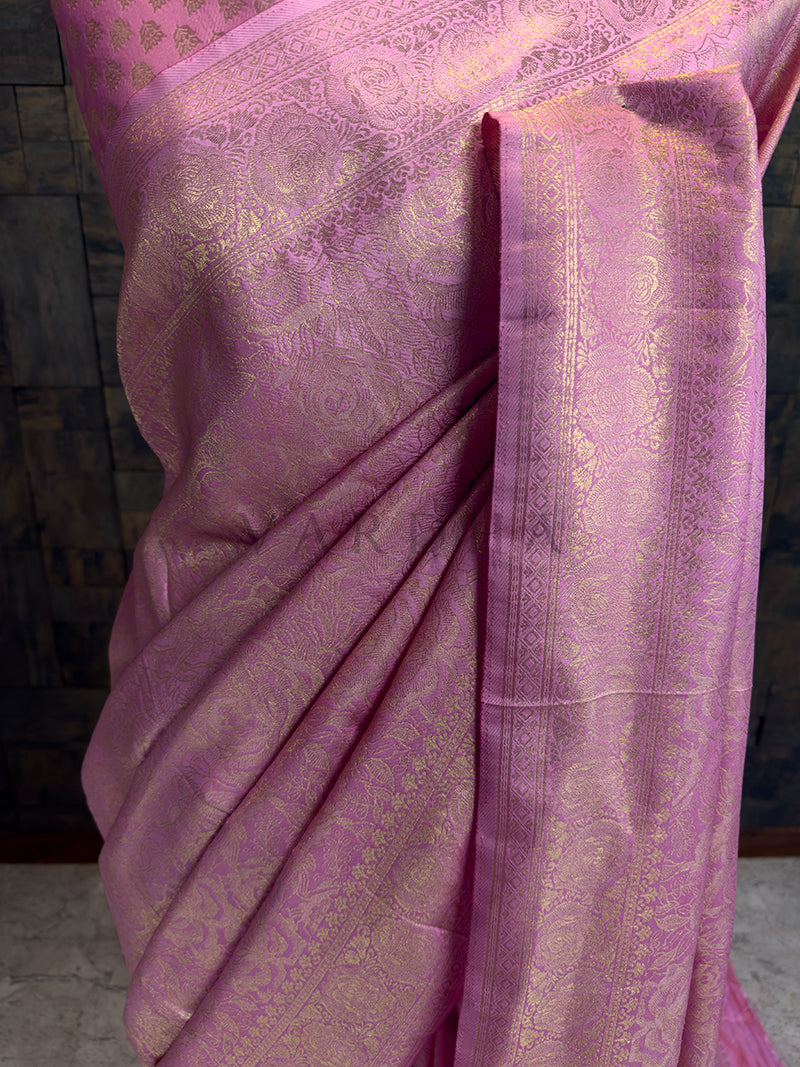 Close-up of House of Vardha Rose Pink Golden Zari Kanjivaram Silk Saree highlighting the detailed gold floral craftsmanship on the pleats. We offer Ready to wear, Pre drape service, Saree Add on, Custom Stitched Blouse, Fall and Edging, Gift Packaging at Complimentary Price!. Pink saree with intricate patterns on a dark background