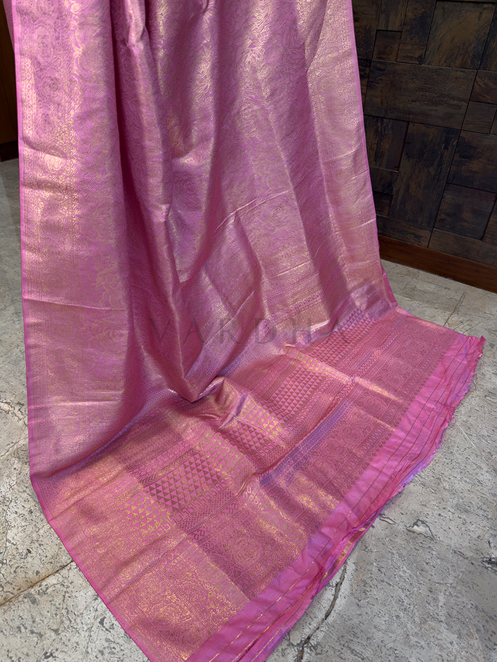 Luxurious authentic Kanjivaram Indian wedding saree in a soft rose pink tone from House of Vardha with extensive gold brocade. We offer Ready to wear, Pre drape service, Saree Add on, Custom Stitched Blouse, Fall and Edging, Gift Packaging at Complimentary Price!. Pink saree draped over a surface with a stone wall background