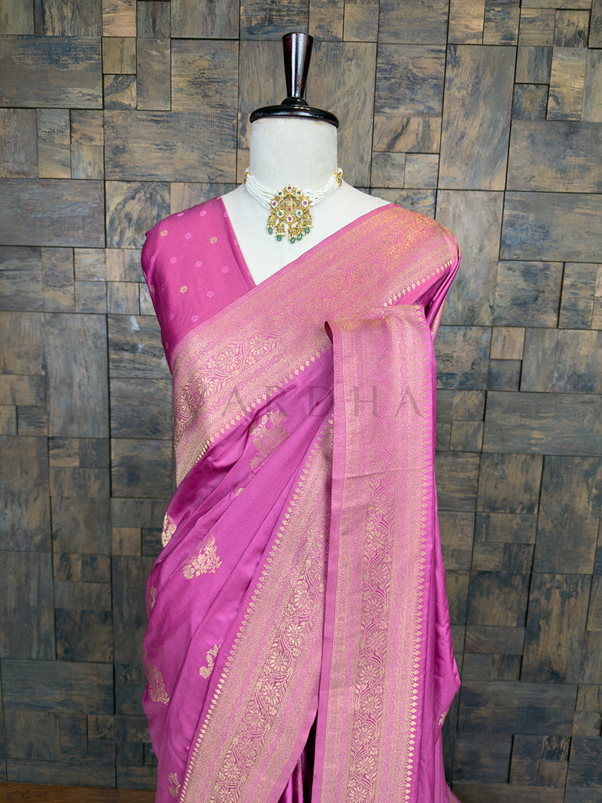 Pink saree with gold border on a mannequin against a textured wall background. Elegant Rose Pink Satin Saree by House of Vardha showcasing intricate Antique Gold Zari Floral Motifs across the body. We offer Ready to wear, Pre drape service, Saree Add on, Custom Stitched Blouse, Fall and Edging, Gift Packaging at Complimentary Price!