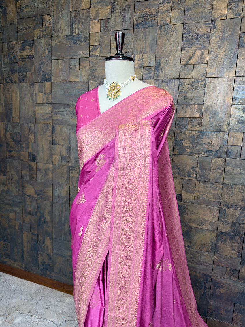 Pink saree with gold border on a mannequin against a textured wall. Close-up of House of Vardha Rose Pink Satin Saree highlighting the detailed Antique Gold Zari Floral Motifs on the pleats and traditional border. We offer Ready to wear, Pre drape service, Saree Add on, Custom Stitched Blouse, Fall and Edging, Gift Packaging at Complimentary Price!