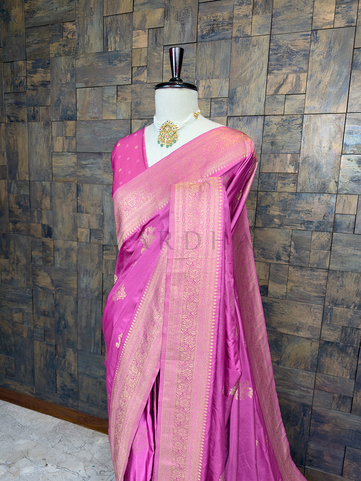 Pink saree with gold border on a mannequin against a textured wall. Close-up of House of Vardha Rose Pink Satin Saree highlighting the detailed Antique Gold Zari Floral Motifs on the pleats and traditional border. We offer Ready to wear, Pre drape service, Saree Add on, Custom Stitched Blouse, Fall and Edging, Gift Packaging at Complimentary Price!