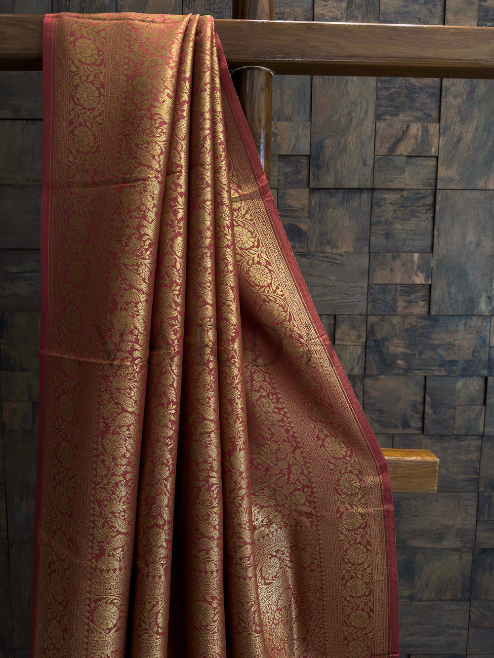 Brown patterned fabric draped over a wooden railing against a stone wall.