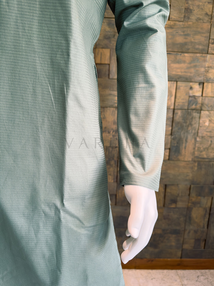 Person wearing a textured blue Kurta with long sleeves against a wooden background. Close-up of the full sleeve and side drape of the textured sage blue cotton kurta, showcasing the breathable premium fabric and clean, elegant contemporary aesthetic.