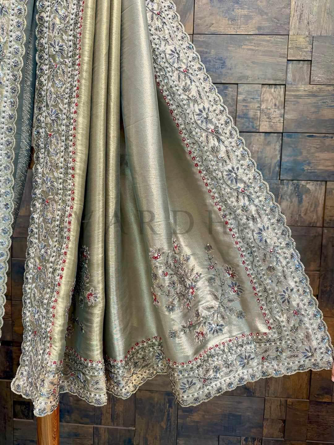 Silk saree with intricate embroidery on a wooden background. Close-up of pallu showing delicate cutdana, stone, and thread embroidery on shimmer base.