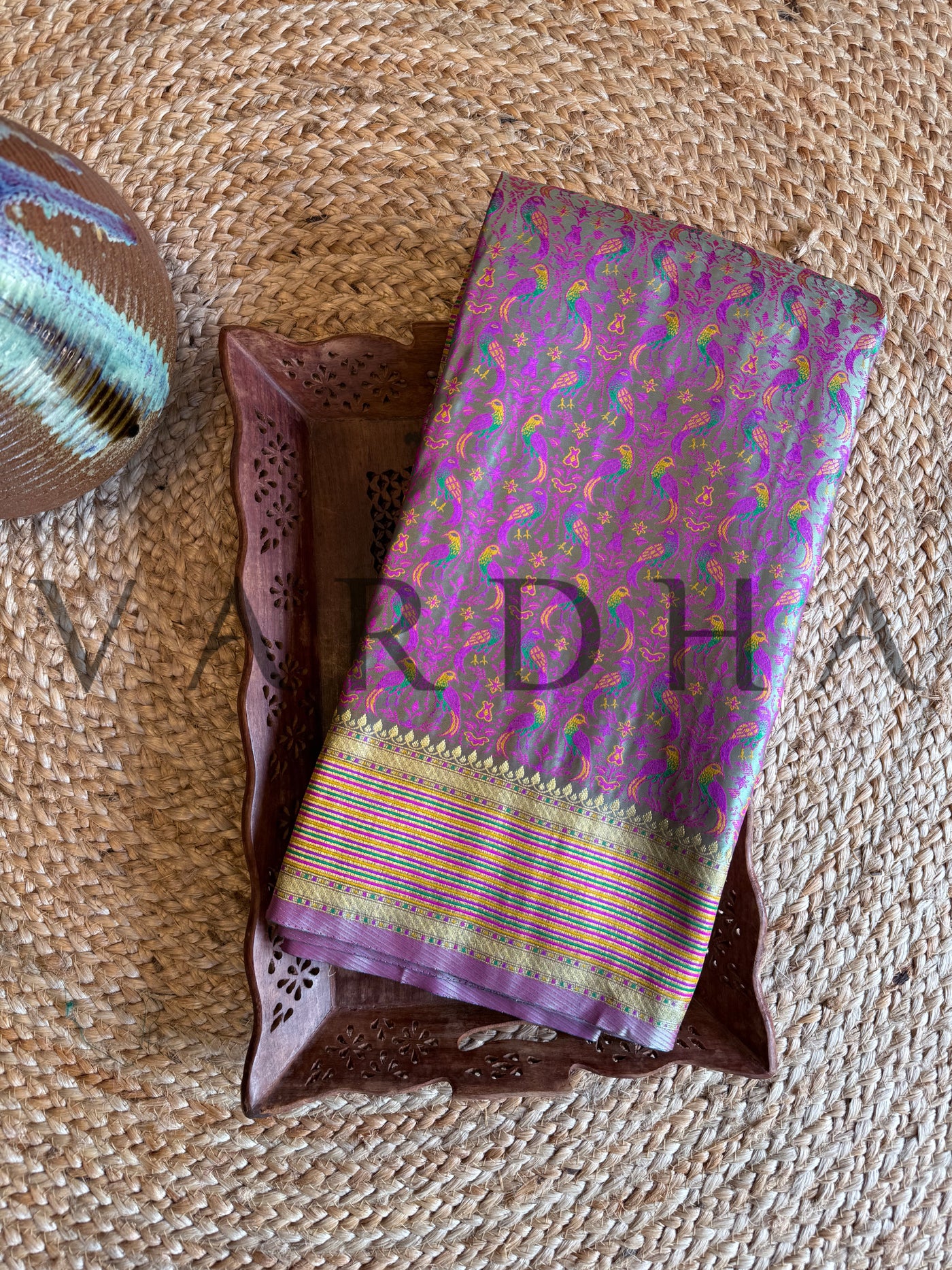 Sea green Tanchoi satin silk saree folded on tray with multicolor thread-woven parrot motifs and golden zari striped border